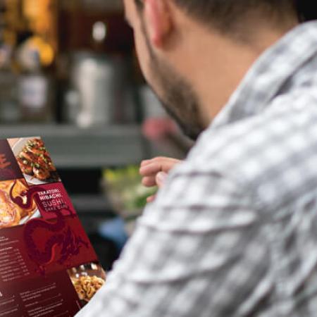 A man reading a restaurant menu that was printed on waterproof, antimicrobial SYNAPS XM synthetic polyester paper.