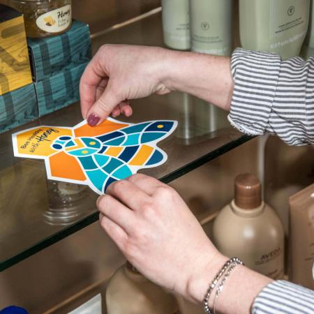 woman installing a premium vinyl graphic to a glass product display shelf